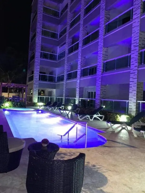 Night view of a lit Ocean Front Lavish Jr Penthouse with lounge chairs and a building facade, highlighted by purple lighting.