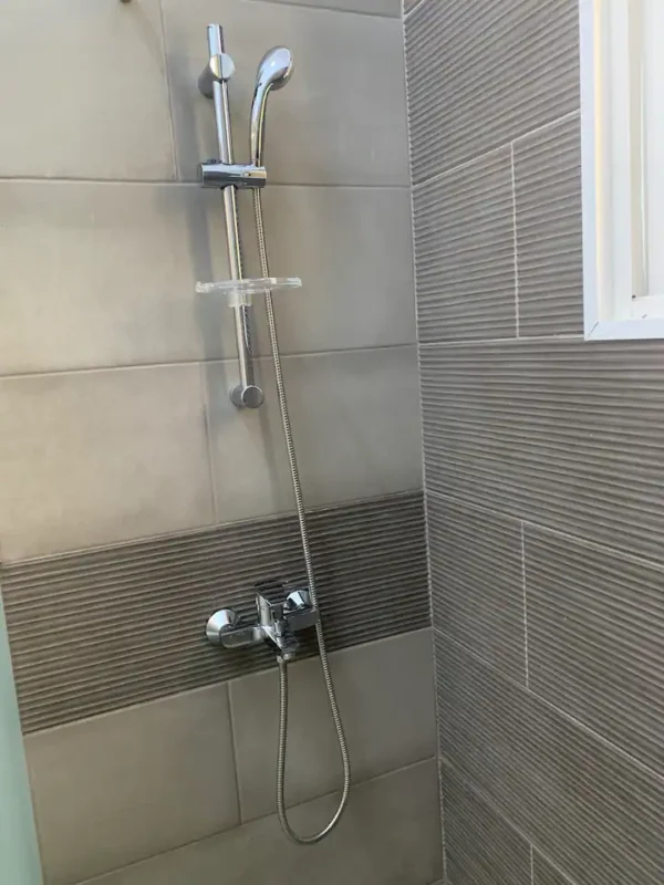 Modern shower with adjustable head and chrome controls mounted on a tiled wall.