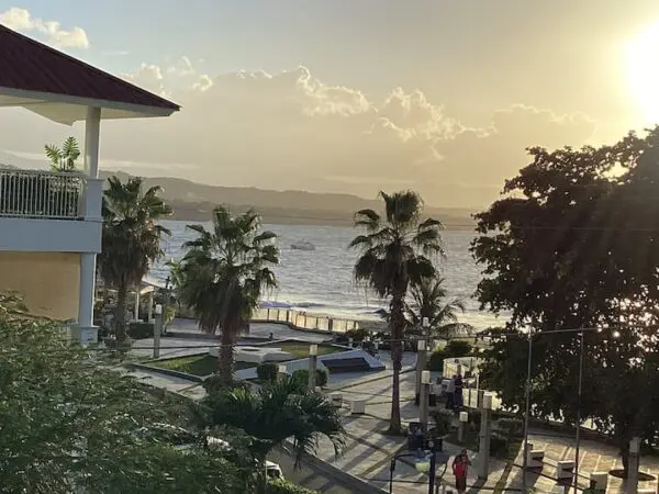 Sunset view over a beachfront promenade with palm trees and a building, highlighting pedestrians and shimmering **Ocean Front Lavish Jr Penthouse Exquisite Views**.