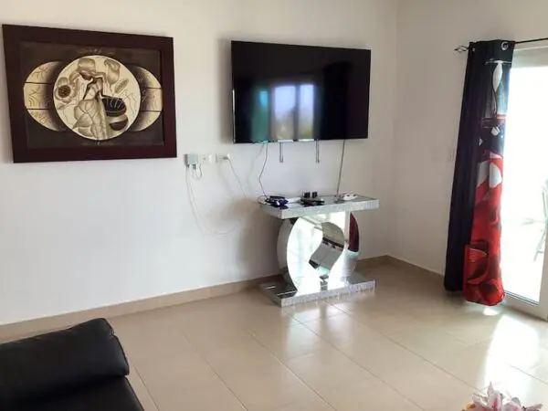 A modern living room with a mounted Ocean Front Lavish *Jr Penthouse* Exquisite Views TV, abstract wall art, a mirrored console table, and a glass door with red patterned curtains.