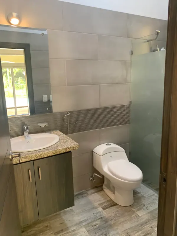 Modern bathroom with beige tiles, featuring a sink with cabinet, toilet, and glass shower enclosure.