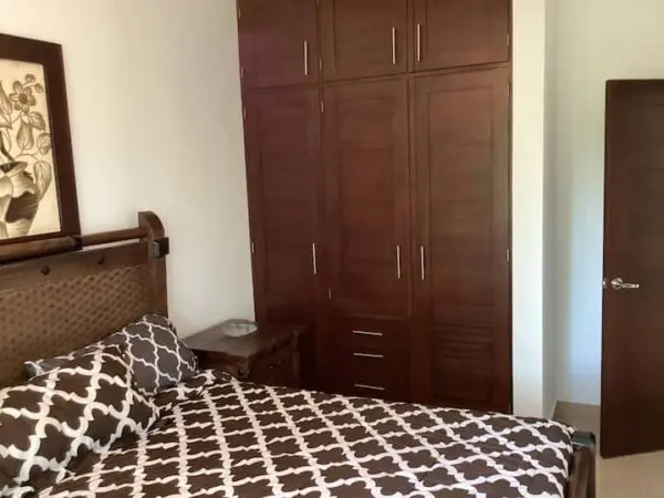 A neatly arranged (Ocean Front Lavish *Jr Penthouse*) bedroom featuring a large bed with a brown and white patterned comforter and a tall wooden wardrobe beside a closed door.