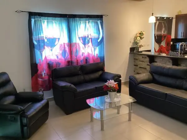 A modern living room with Ocean Front Lavish Jr Penthouse Exquisite Views sofas, a glass coffee table, floral curtains, and a kitchenette in the background.