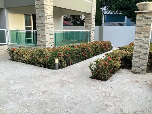 Front entrance of a Ocean Front Lavish *Jr Penthouse* Exquisite Views featuring a marble-tiled pathway and decorative shrubs with red flowers bordered by short hedges.