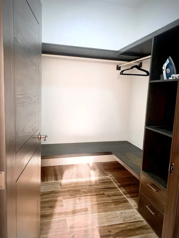 Empty walk-in closet with wooden flooring, built-in shelves, and bright lighting.