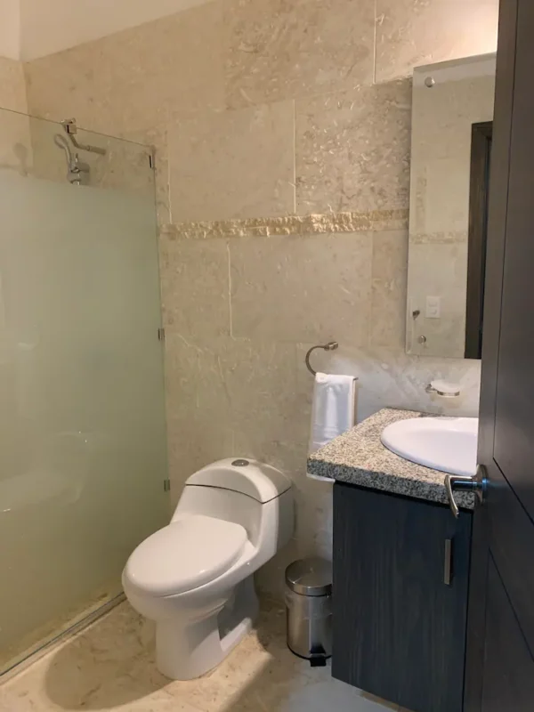 A compact bathroom featuring a toilet, shower with glass door, sink with granite countertop, and a mirror, all in beige tones.