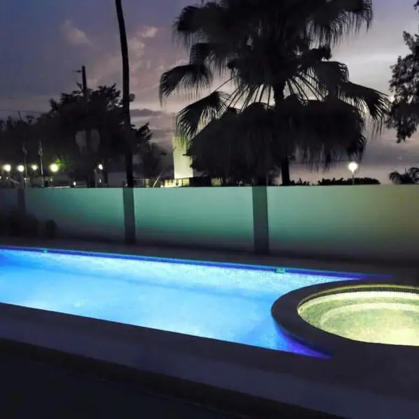 A Ocean Front Lavish *Jr Penthouse* Exquisite Views illuminated with blue lights under a twilight sky, featuring palm trees and a low wall in the background.