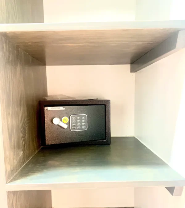 A small safe with a digital keypad and a white fob on top, placed inside a wooden cubby shelf.