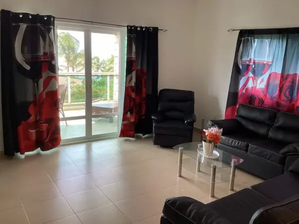 Modern living room with black leather Ocean Front Lavish *Jr Penthouse* Exquisite Views, red floral curtains, and a view of a balcony overlooking a bright exterior.