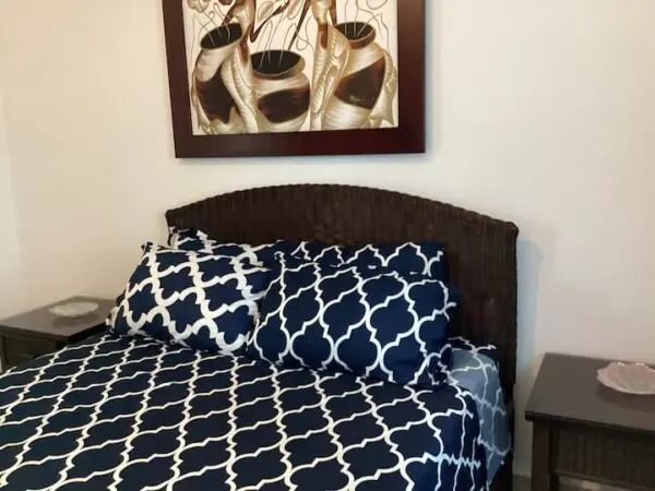 A neatly made bed with Ocean Front Lavish Jr Penthouse Exquisite Views bedding, a woven headboard, and a framed abstract art piece above it.