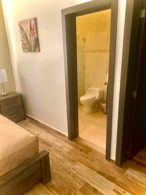 Interior view of a bedroom with an adjacent open bathroom door, showing a toilet and tiled walls.