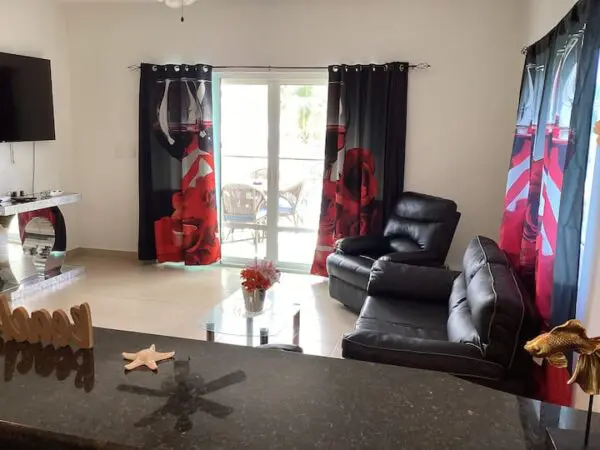 A modern living room with black leather Ocean Front Lavish *Jr Penthouse* Exquisite Views sofa, red patterned curtains, glass coffee table, and coastal decor elements.