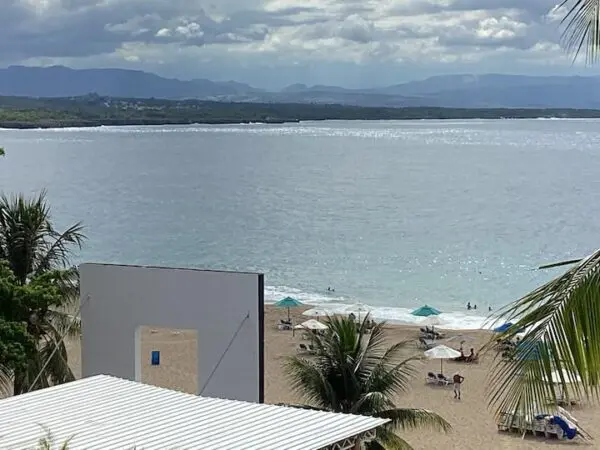 View of a beach with people and umbrellas, overlooking a tranquil sea and distant mountains, with Ocean Front Lavish *Jr Penthouse* Exquisite Views in the foreground.