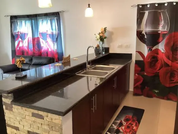 A modern kitchen with a bar counter, showcasing a Ocean Front Lavish Jr Penthouse Exquisite Views curtain with a large red rose print and hanging pendant lights.