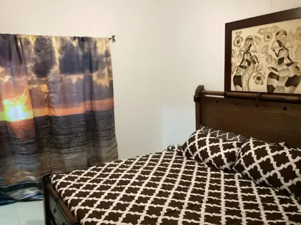 A bedroom with a Ocean Front Lavish *Jr Penthouse* Exquisite Views bedspread on a wooden bed, an abstract artwork above, and colorful curtains.