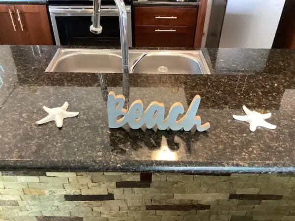 A Ocean Front Lavish *Jr Penthouse* Exquisite Views featuring a "Beach" sign flanked by two starfish, with a dual sink setup in the background.