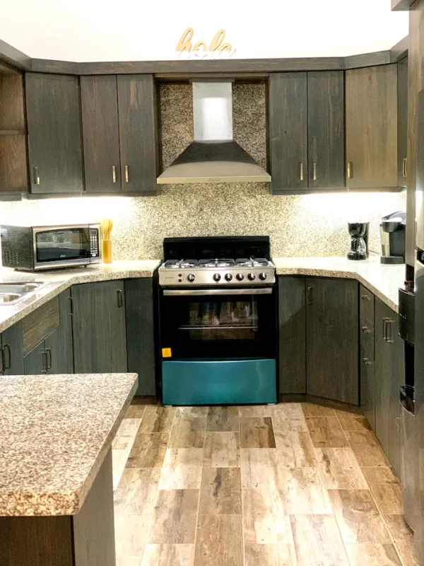 A modern kitchen with dark wood cabinetry, granite countertops, and stainless steel appliances, including a teal oven.