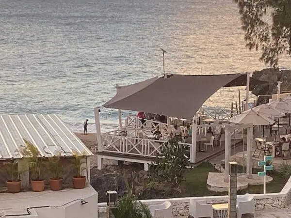 Outdoor seaside restaurant with tables under a large canopy and a person walking along the adjacent beach at sunset at Ocean Front Lavish *Jr Penthouse* Exquisite Views.