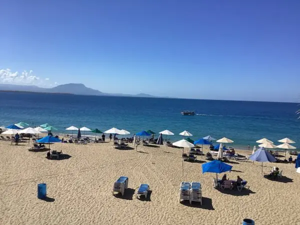 Ocean Front Lavish *Jr Penthouse* Exquisite Views lined with umbrellas and lounge chairs, overlooking a clear blue sea with a distant mountain.