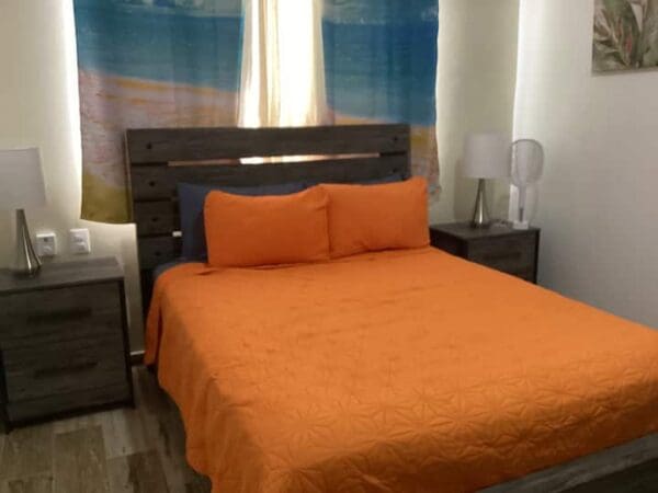 A bed with an orange bedspread and pillows.