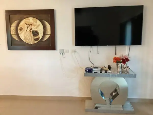 A living room wall featuring Ocean Front Lavish *Jr Penthouse* Exquisite Views above a modern console table, with a flat-screen TV to the right and decorative flowers on the table.