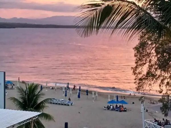 Sunset over a beach with people, palm trees, and Ocean Front Lavish *Jr Penthouse* Exquisite Views reflecting golden hues.