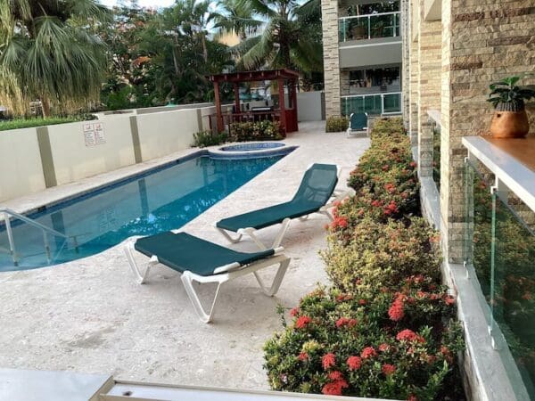 Outdoor pool area with two lounge chairs, surrounded by lush plants and adjacent to an Ocean Front Lavish Jr Penthouse Exquisite Views.