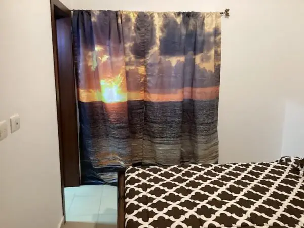 A bedroom with a Ocean Front Lavish *Jr Penthouse* Exquisite Views covered in a brown and white patterned duvet and a window with a sunset-themed curtain.