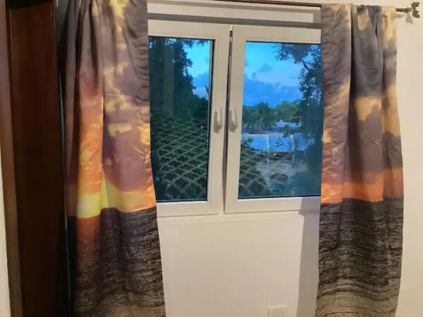 A window with Ocean Front Lavish *Jr Penthouse* Exquisite Views curtains open, showing a view of trees and a sky reflected in a body of water outside.