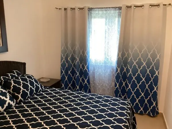 A small bedroom with a patterned Ocean Front Lavish *Jr Penthouse* Exquisite Views duvet on a bed, flanked by curtains with a matching blue pattern, with soft light filtering through a window.