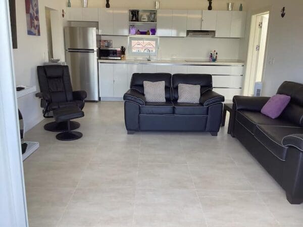 A living room with black leather furniture and white tile flooring.