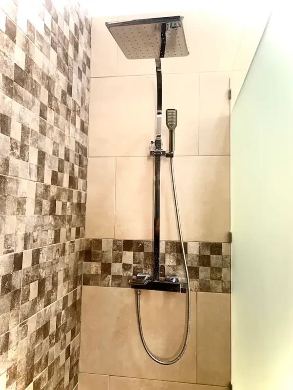 Modern shower with a large square shower head and a handheld sprayer, surrounded by brown and beige tiled walls.