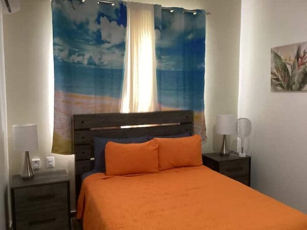 A bedroom with an orange bed and blue sky curtains.