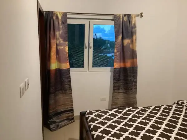 A bedroom with a Ocean Front Lavish *Jr Penthouse* Exquisite Views, covered in a black and white patterned duvet, and a window with curtains showing a twilight sky.