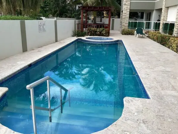 Ocean Front Lavish Jr Penthouse with clean blue water, entry steps with metal handrail, surrounded by a white fence and adjacent building.