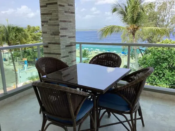 Patio with a dining table and four wicker chairs overlooking a tropical beach and ocean view from Ocean Front Lavish *Jr Penthouse* Exquisite Views framed by palm trees.