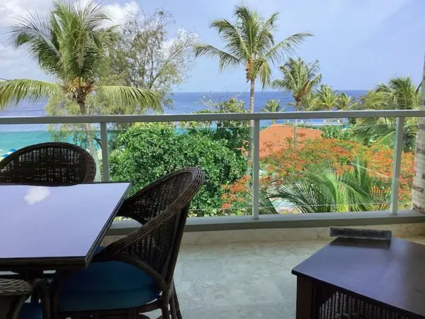 Balcony view of a tropical seaside featuring palm trees and Ocean Front Lavish *Jr Penthouse* Exquisite Views, with a table and chairs set up for a scenic meal.