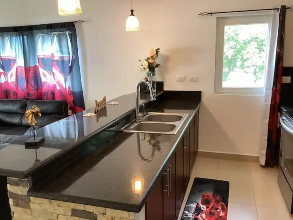 A modern kitchen with an Ocean Front Lavish *Jr Penthouse* Exquisite Views countertop, stainless steel sink, and red-accented curtains and decor.