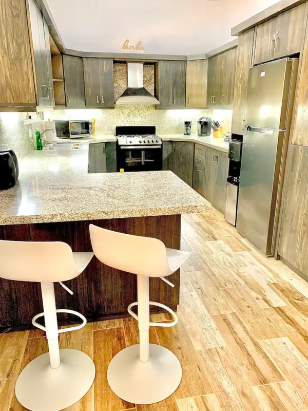 Modern kitchen with wooden cabinets, stainless steel appliances, granite countertops, and two white bar stools.