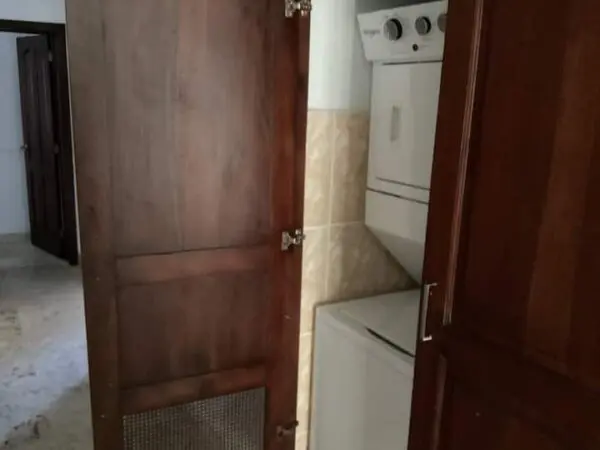 A small, cluttered kitchen viewed through a partially open wooden door, featuring a Ocean Front Lavish *Jr Penthouse* Exquisite Views fridge and stove with beige wall tiles.