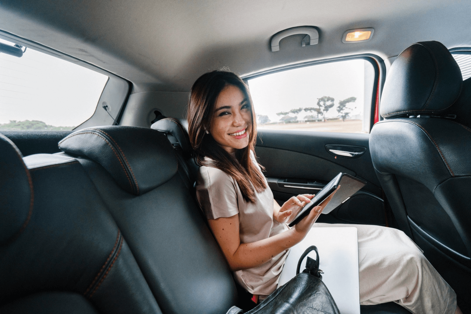 A woman sitting in the back of a car holding her tablet.