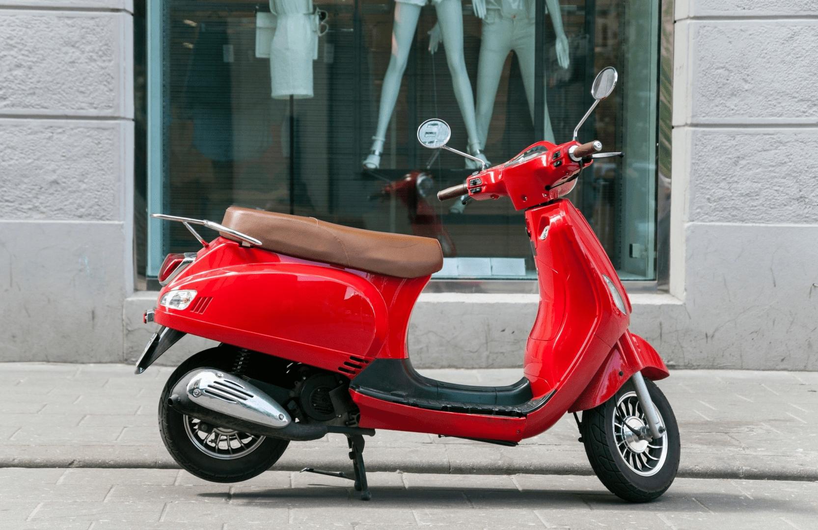 A red scooter parked on the side of a street.